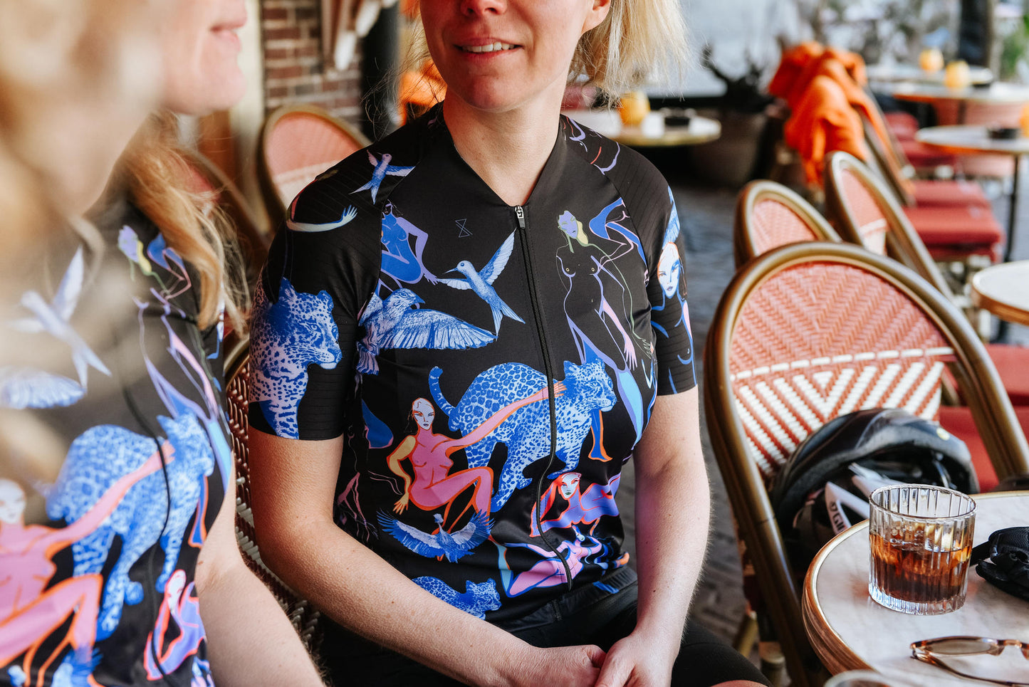 Twee dames op het terras beide gekleed in het fietsshirt zwart met print met korte mouwen van TENUE des Femmes.