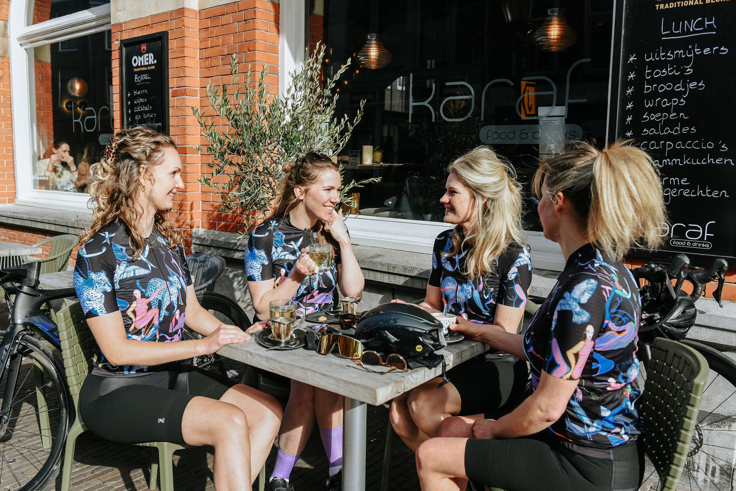 Groep vrouwen op het terras allemaal gekleed in het fietsshirt zwart met print, korte mouwen van TENUE des Femmes de imited edition genaamd Unlimited Femmes