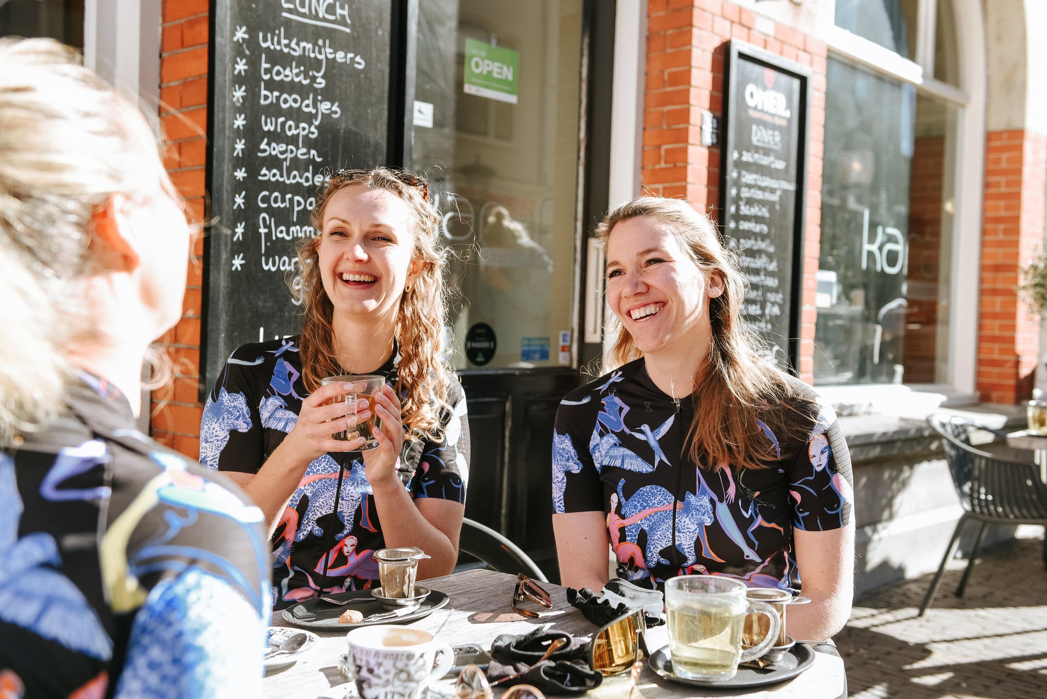 Dames tijdens een koffiestop van een wielrenrit gekleed in een wielershirt met korte mouwen voor vrouwen. Alle dames dragen de Limited Edition van TENUE des Femmes, Unlimted Femmes 